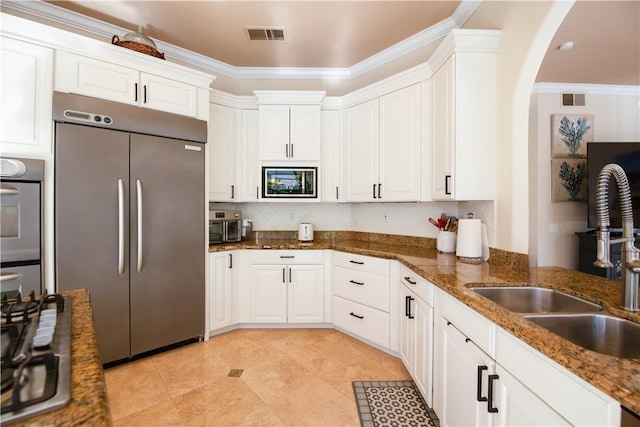 kitchen with ornamental molding, a sink, white cabinetry, dark stone counters, and built in appliances