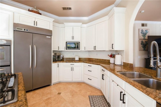 kitchen with white cabinetry, ornamental molding, built in appliances, and a sink