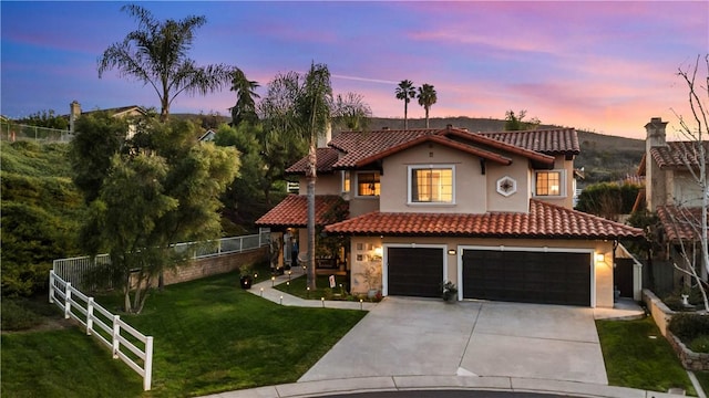 mediterranean / spanish home featuring fence, a tile roof, concrete driveway, a front yard, and stucco siding