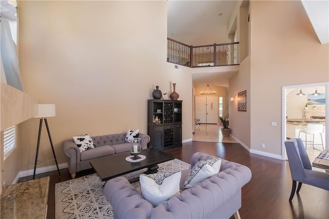 living area with plenty of natural light, wood finished floors, baseboards, and a towering ceiling