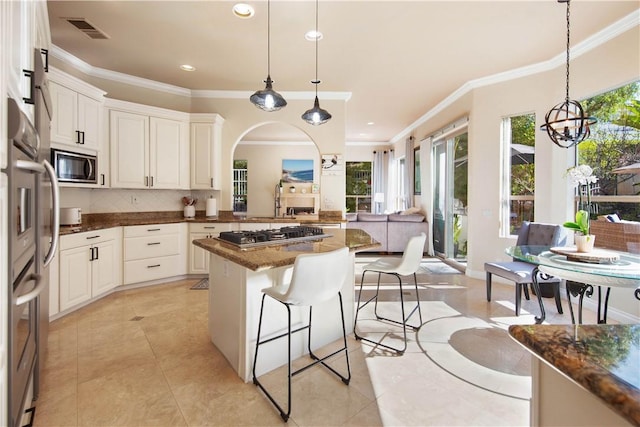 kitchen featuring visible vents, backsplash, a breakfast bar area, built in microwave, and stainless steel gas cooktop