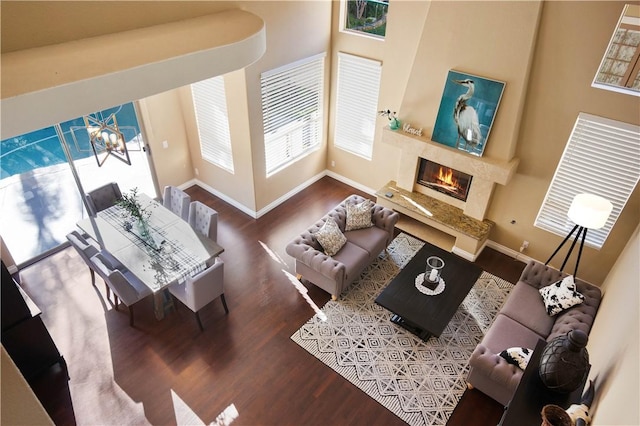 living room with wood finished floors, a fireplace, baseboards, and a towering ceiling