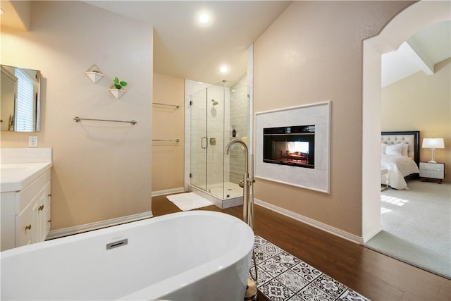 bathroom featuring a shower stall, a freestanding bath, a fireplace, wood finished floors, and vanity