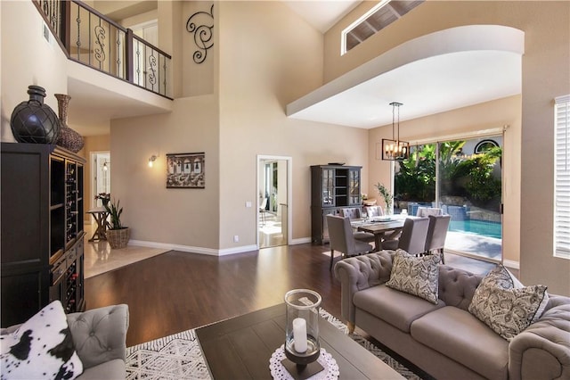 living room featuring a high ceiling, a notable chandelier, wood finished floors, and baseboards