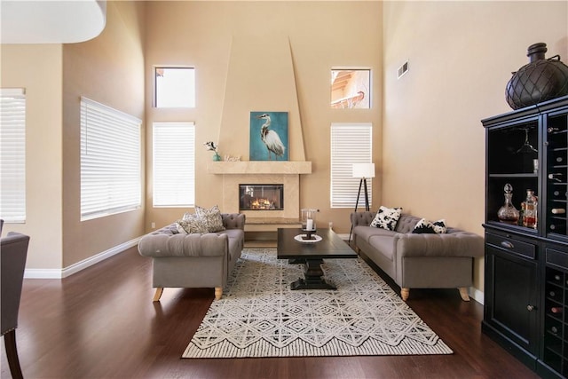 living room featuring visible vents, a large fireplace, baseboards, dark wood finished floors, and a high ceiling