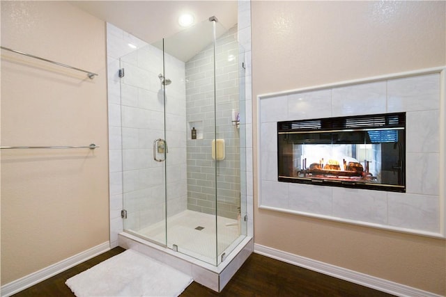 full bathroom with lofted ceiling, a stall shower, wood finished floors, baseboards, and a tile fireplace