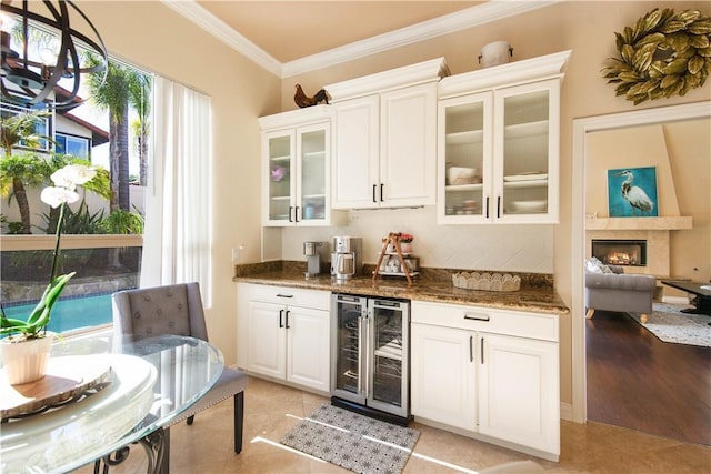 bar featuring light tile patterned floors, a lit fireplace, beverage cooler, and crown molding