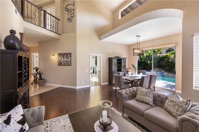 living area with a chandelier, baseboards, a high ceiling, and dark wood-style floors