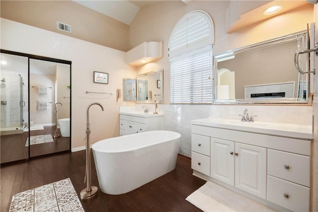 bathroom featuring visible vents, two vanities, a stall shower, a sink, and wood finished floors