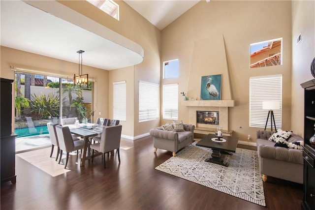 living room with baseboards, a fireplace, wood finished floors, a notable chandelier, and high vaulted ceiling