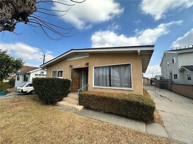 bungalow-style home with stucco siding, a front lawn, and fence