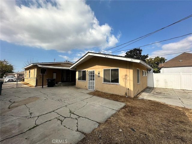 back of house featuring a carport, stucco siding, a patio, and fence