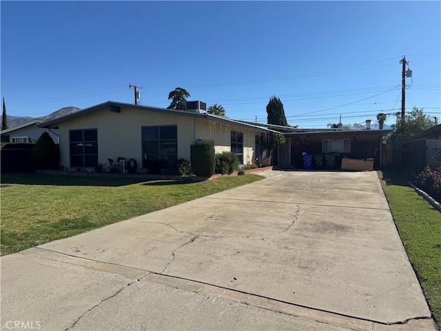 ranch-style house featuring stucco siding, driveway, a front lawn, and fence