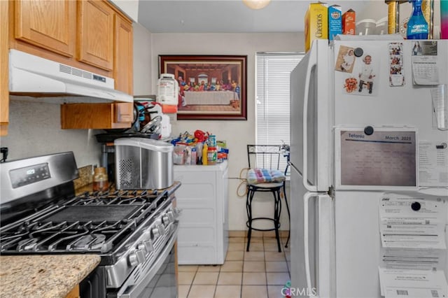 kitchen with under cabinet range hood, freestanding refrigerator, gas stove, light tile patterned flooring, and light countertops