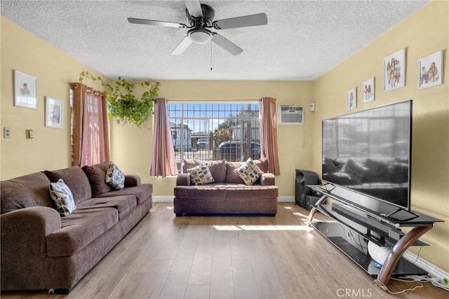 living room featuring a ceiling fan, an AC wall unit, wood finished floors, and a textured ceiling