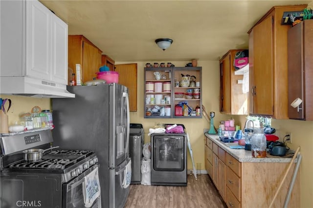 kitchen with stainless steel gas range, light countertops, under cabinet range hood, light wood-type flooring, and washer and clothes dryer