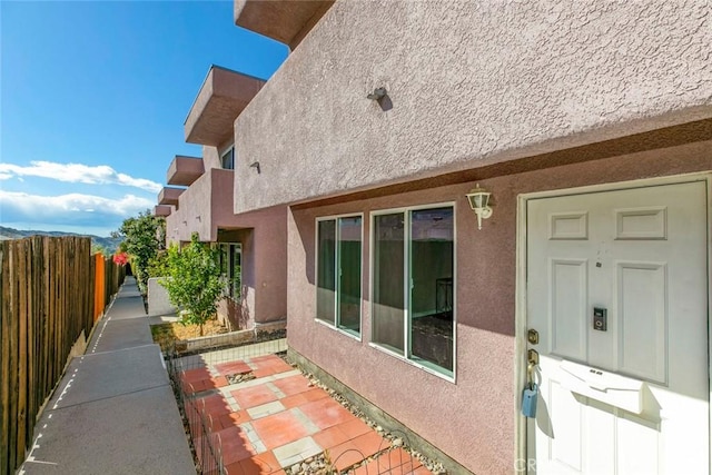 doorway to property featuring stucco siding and fence