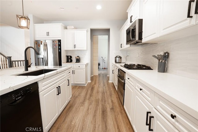 kitchen with light wood-type flooring, hanging light fixtures, white cabinets, black appliances, and a sink