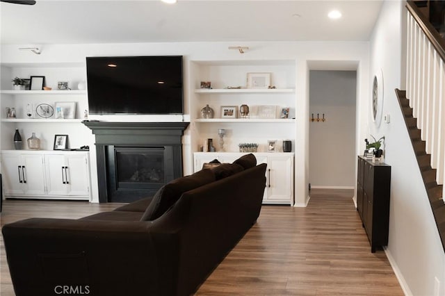 living room with stairway, built in features, wood finished floors, baseboards, and a glass covered fireplace