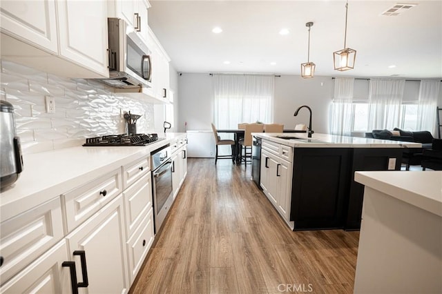 kitchen featuring visible vents, light wood finished floors, a sink, stainless steel appliances, and backsplash