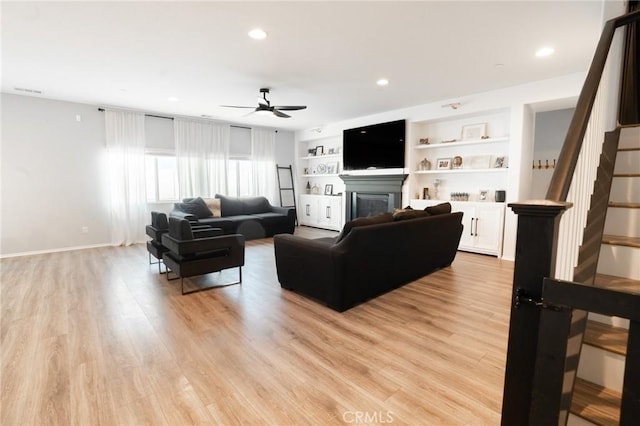 living room featuring stairway, built in features, light wood-type flooring, recessed lighting, and a glass covered fireplace