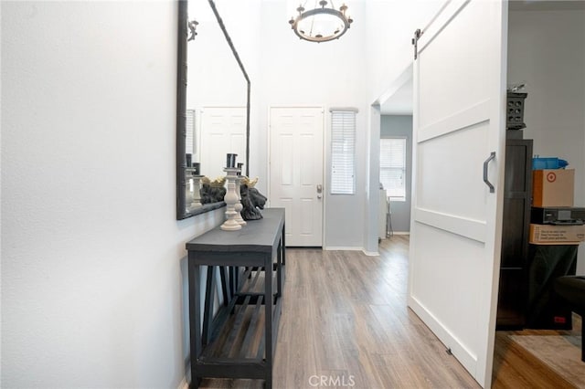 foyer entrance featuring a barn door, baseboards, a high ceiling, and light wood-style flooring