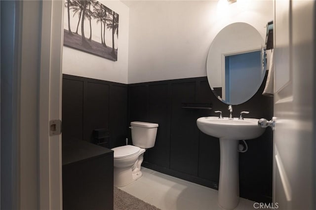 half bathroom featuring a decorative wall, wainscoting, and toilet