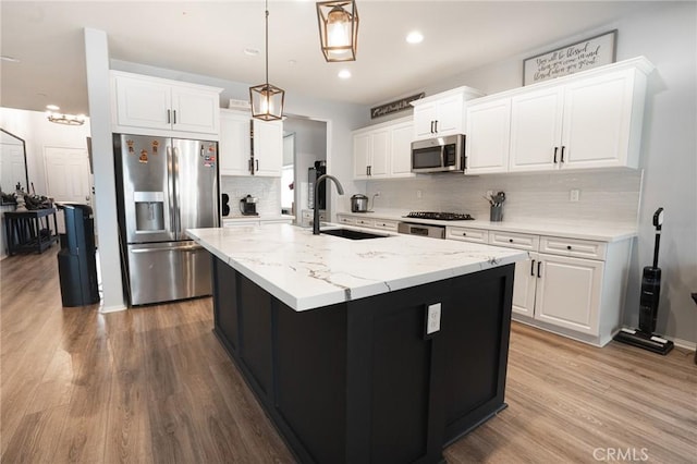 kitchen featuring a sink, stainless steel appliances, wood finished floors, white cabinetry, and a kitchen island with sink