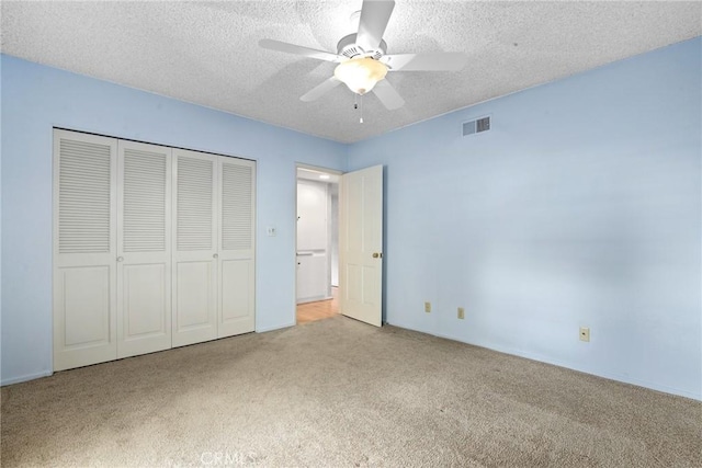 unfurnished bedroom with visible vents, carpet floors, ceiling fan, a closet, and a textured ceiling