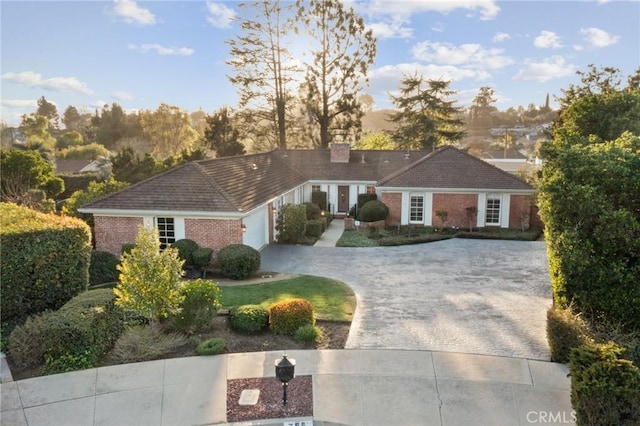 view of front of home featuring decorative driveway, brick siding, a garage, and a chimney