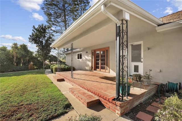 entrance to property featuring stucco siding, a yard, french doors, and a patio area