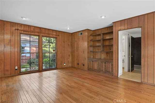 spare room featuring wooden walls, visible vents, built in shelves, and light wood-style floors