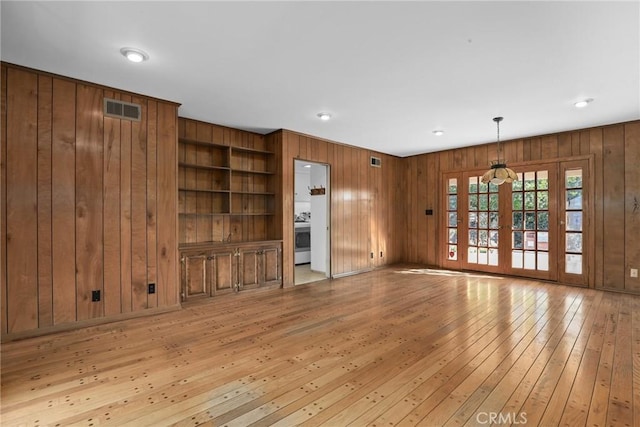 unfurnished living room featuring built in features, visible vents, light wood finished floors, french doors, and wood walls