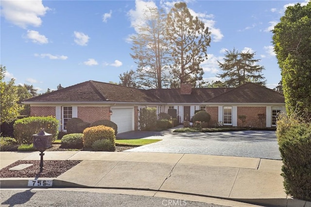 ranch-style home with brick siding, a tile roof, a chimney, a garage, and driveway