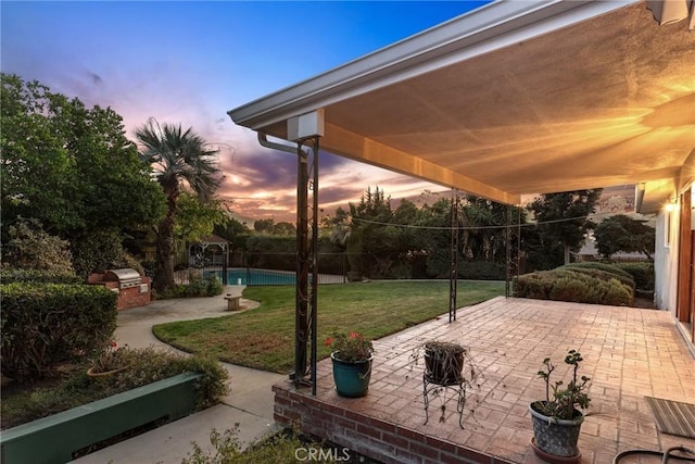 patio terrace at dusk with a fenced in pool, an outdoor kitchen, a yard, and fence