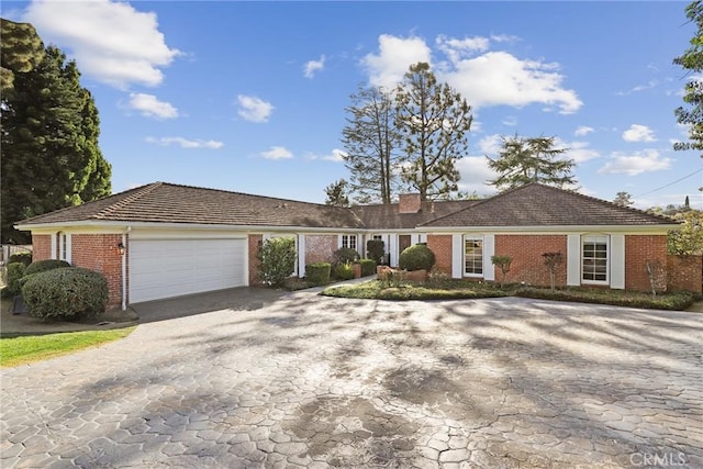 single story home with decorative driveway, brick siding, a chimney, and an attached garage