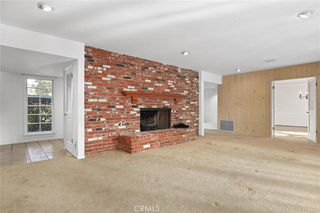 unfurnished living room with tile patterned floors, visible vents, carpet, wood walls, and a fireplace