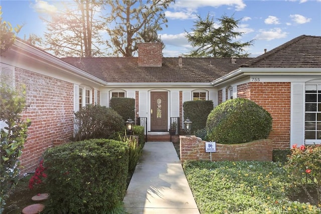 view of exterior entry featuring brick siding and a chimney