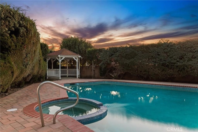 pool at dusk with a gazebo, a pool with connected hot tub, and fence