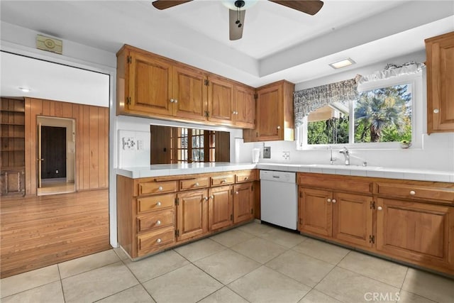 kitchen with light tile patterned floors, brown cabinets, white dishwasher, a ceiling fan, and a sink