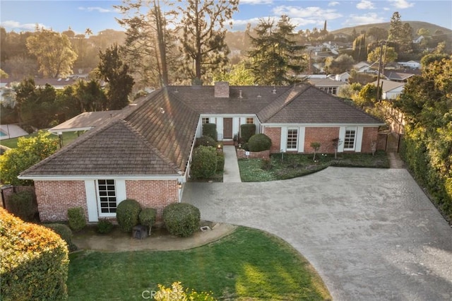 view of front of property featuring brick siding, fence, a front yard, a chimney, and driveway