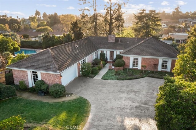 ranch-style house featuring driveway, a front yard, a garage, brick siding, and a chimney