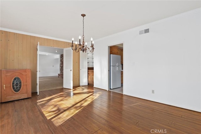 unfurnished dining area featuring visible vents, crown molding, an inviting chandelier, and wood-type flooring