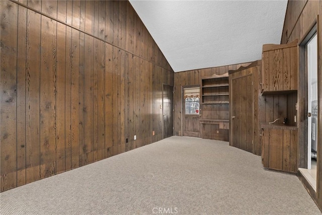 spare room featuring vaulted ceiling, carpet, wood walls, and a textured ceiling