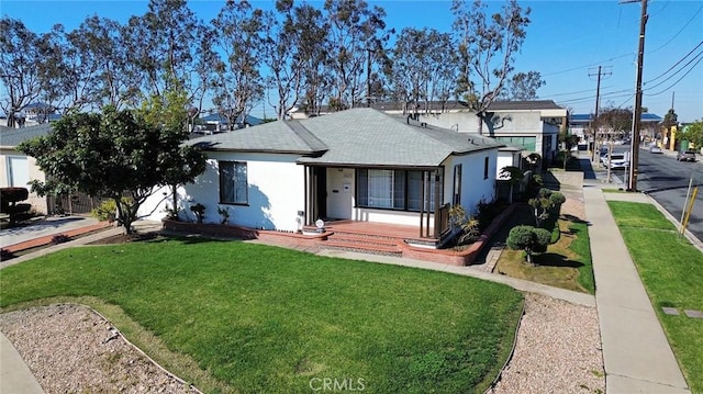 view of front of home with stucco siding, a shingled roof, and a front yard