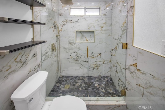 bathroom featuring a marble finish shower, toilet, and tile walls