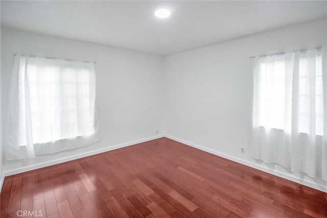 spare room featuring plenty of natural light, wood finished floors, and baseboards