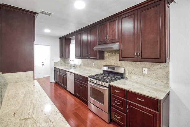 kitchen with dark wood finished floors, a sink, under cabinet range hood, appliances with stainless steel finishes, and tasteful backsplash