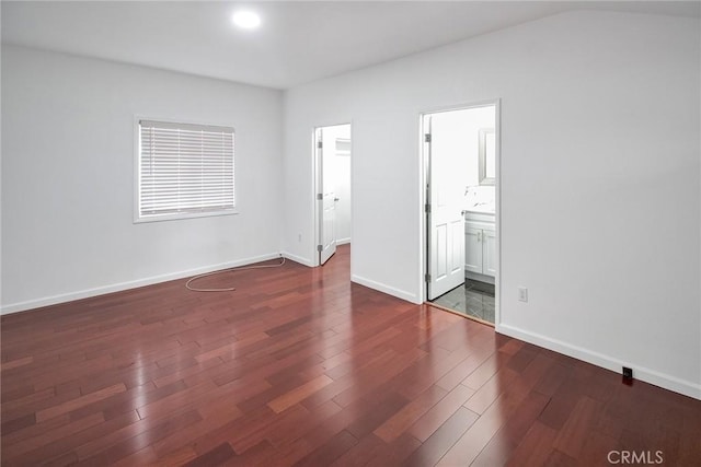 unfurnished bedroom featuring baseboards, a spacious closet, ensuite bathroom, and dark wood-style flooring