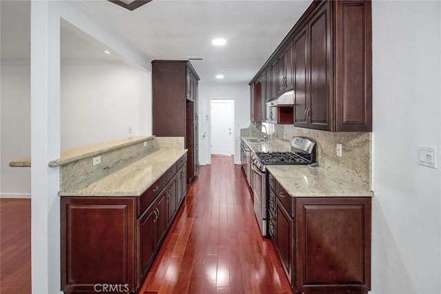 kitchen featuring a sink, under cabinet range hood, decorative backsplash, stainless steel gas stove, and dark wood-style flooring